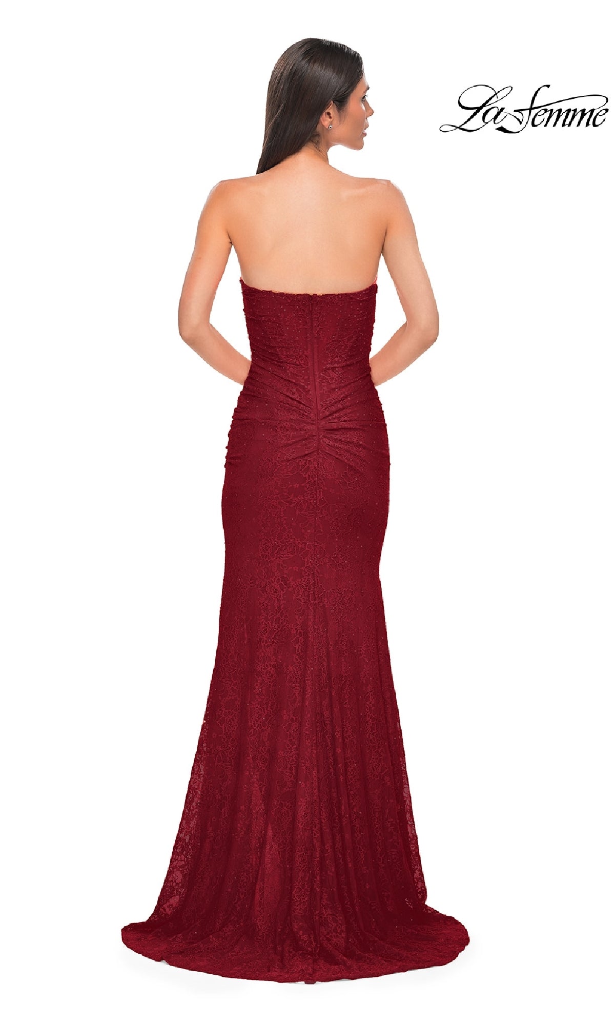 A woman faces away from the camera in a fitted, strapless La Femme 32773 long beaded prom dress. The floor-length gown in red features ruching at the back. The La Femme logo is visible in the top right corner.